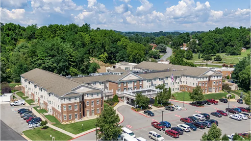 Aerial view of a modern building surrounded by greenery and a parking area.