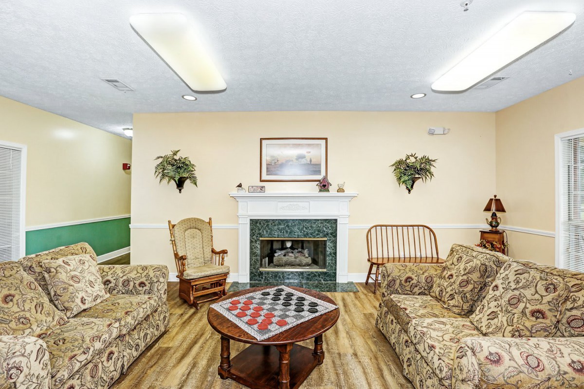 A cozy living room with a fireplace, sofas, rocking chair, and a chessboard on the coffee table.