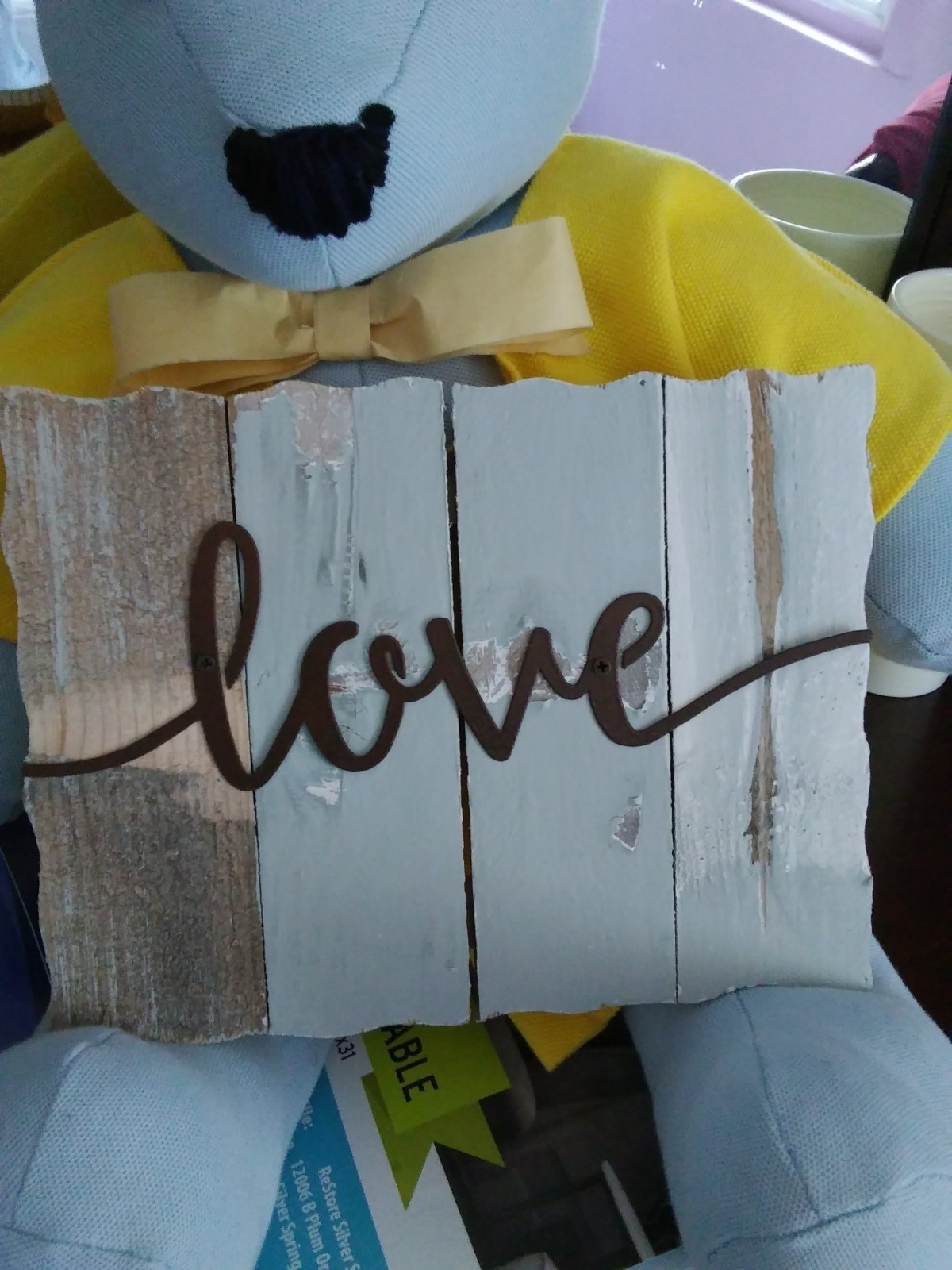 A decorative pillow with 'love' written on a wooden sign, accompanied by a plush toy.