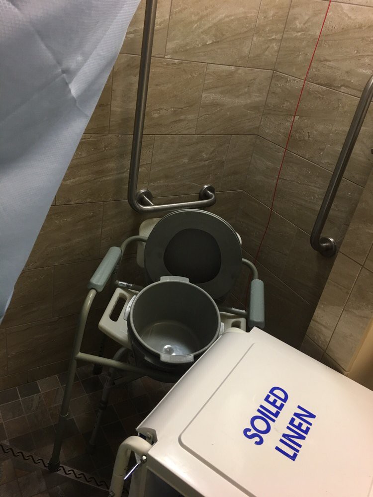 A bathroom equipped with a commode chair, bucket, and cooler.