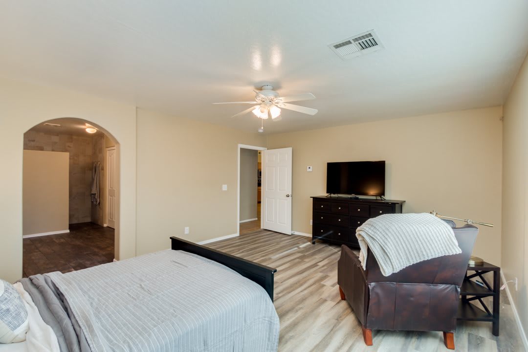 A spacious bedroom with a ceiling fan, featuring a bed, dresser, and television.