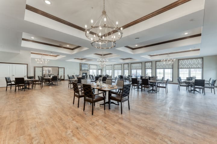A spacious dining room with elegant chandeliers, arranged tables, and wooden flooring.