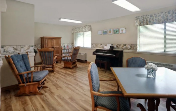 A cozy living room with a piano, wooden chairs, and a bookshelf.