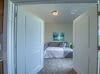 A cozy bedroom viewed through an open doorway, featuring a neatly made bed and minimalist decor.