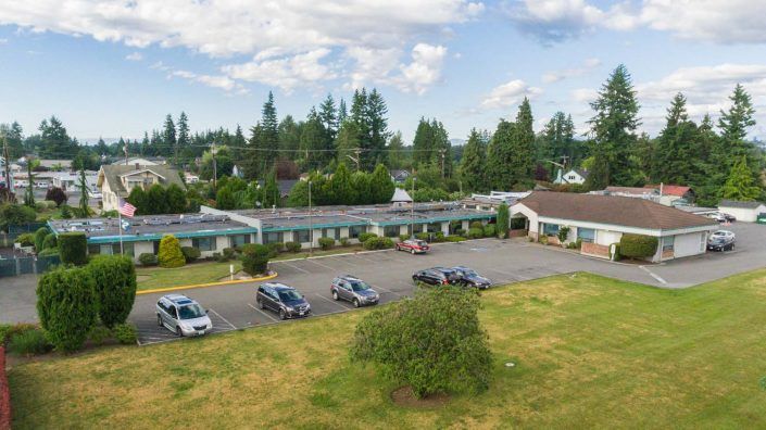Aerial view of a motel with a parking lot and several cars, surrounded by trees under a cloudy sky.