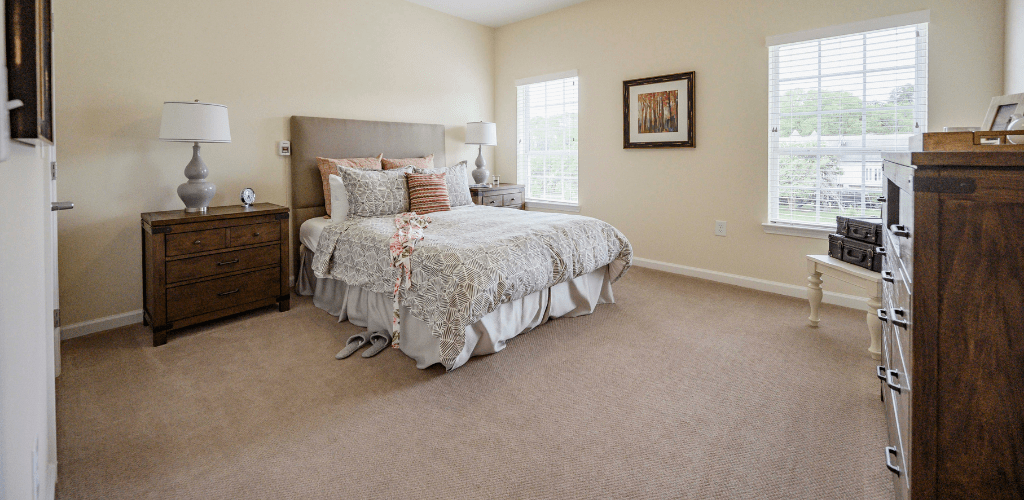 A cozy bedroom interior featuring a neatly made bed, carpeted floor, and elegant decor.