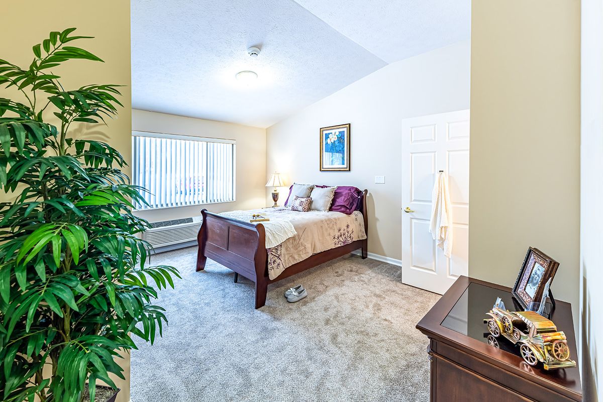 A cozy bedroom with a wooden bed, plush carpet, and natural light from a large window.