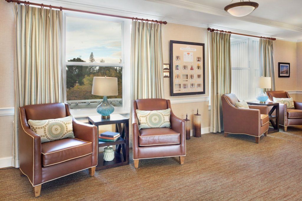 A cozy living room with leather chairs, large windows, and a lamp on a side table.