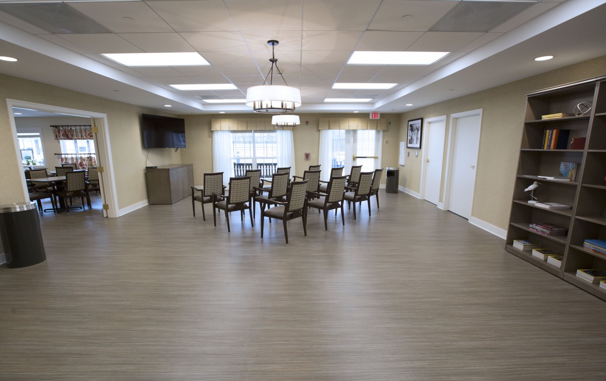 A modern meeting room with a central table, surrounded by chairs and illuminated by overhead chandeliers.