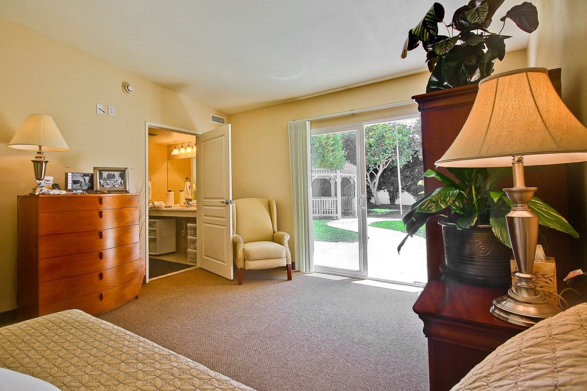 A cozy bedroom with natural light streaming through a sliding door, featuring an armchair and warm decor.