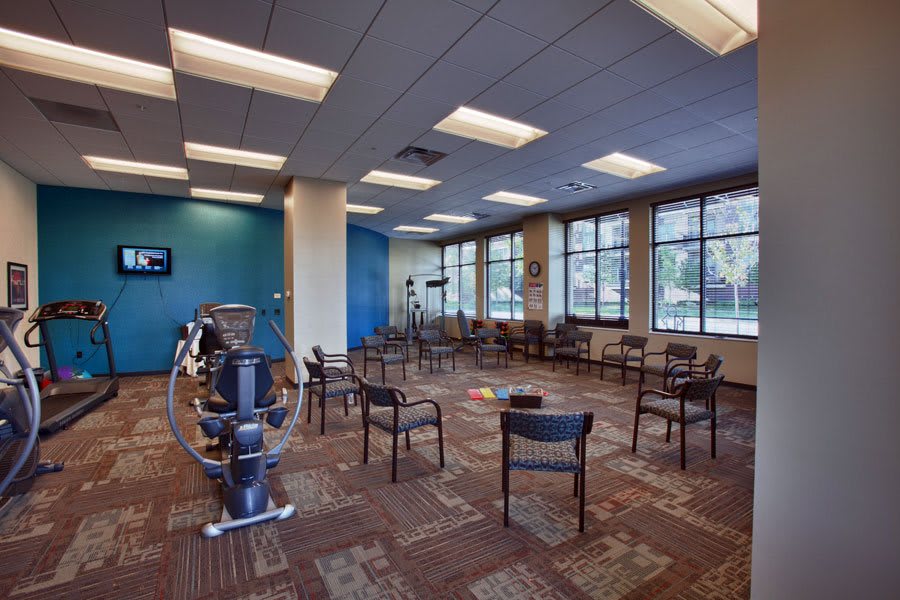 A spacious gym with exercise equipment and arranged chairs near large windows.