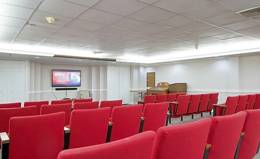 Empty conference room with red chairs and a projector screen.