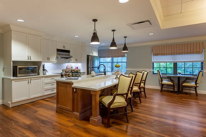 A modern kitchen featuring an island with bar stools, pendant lighting, and wood flooring.