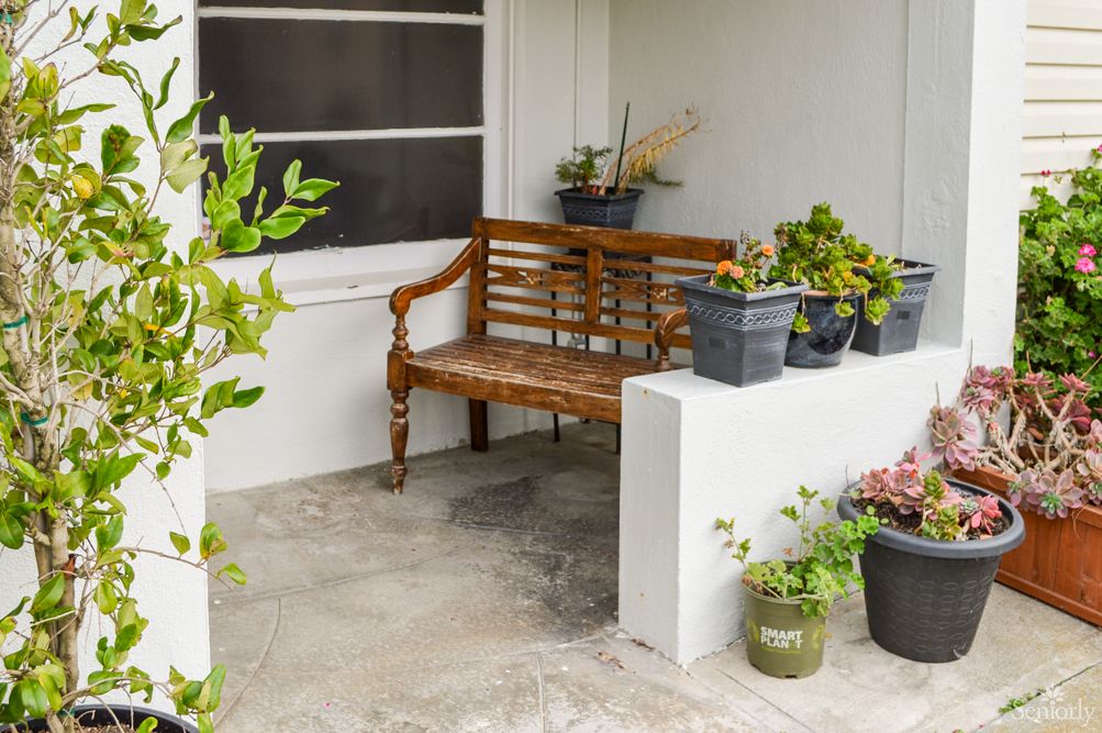 A cozy outdoor patio with a wooden bench and decorative plant pots.