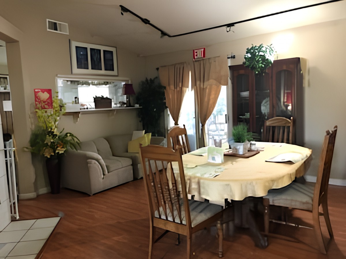 Cozy dining area with a wooden table and chairs, decorated with plants and curtains.