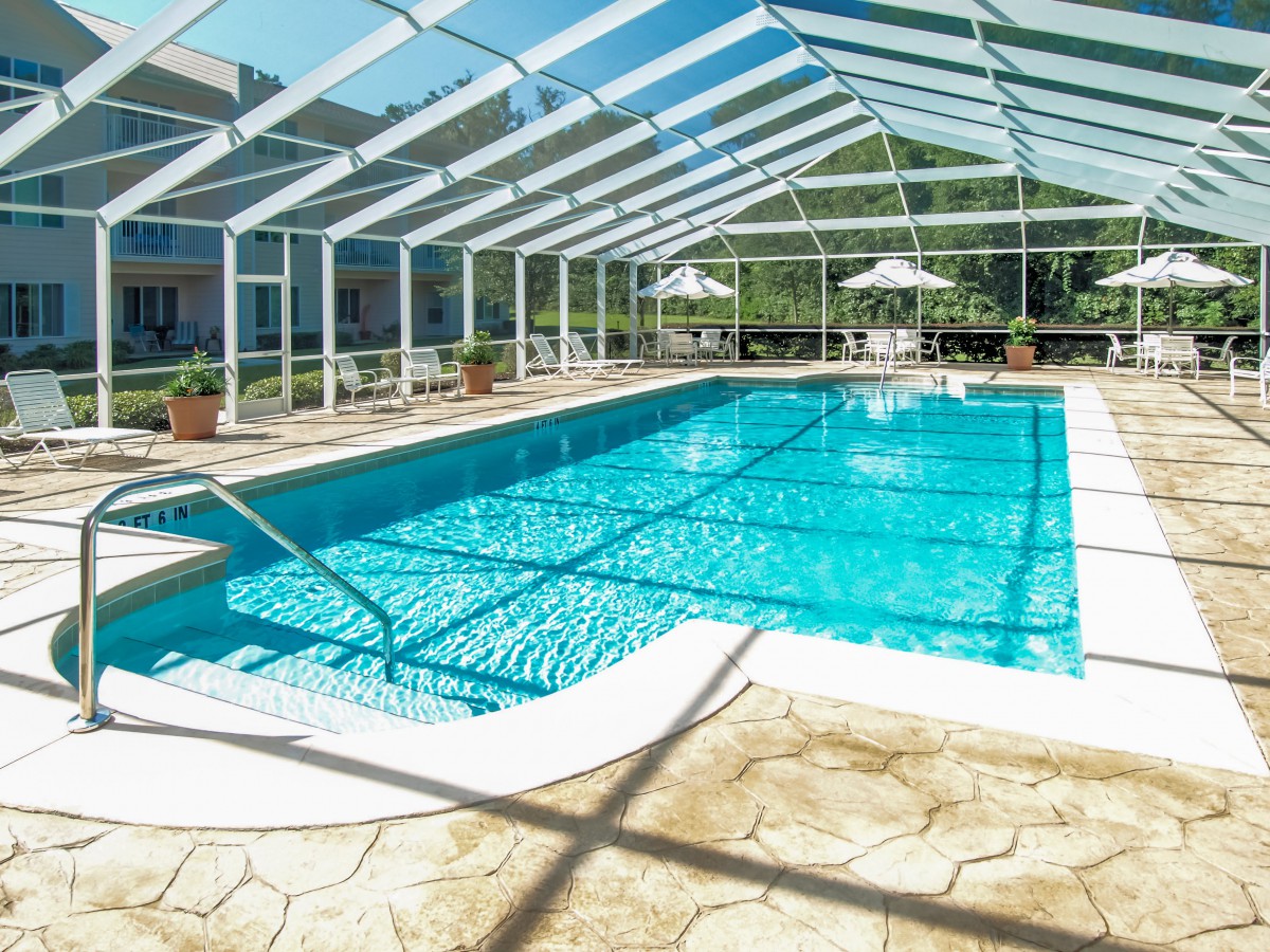A sunlit indoor swimming pool enclosed in a glass structure, offering a serene and relaxing environment.