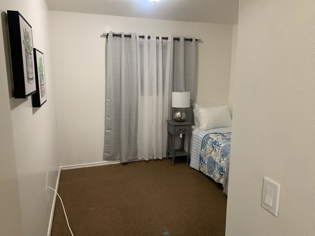 A minimalist bedroom with a single bed, bedside lamp, and light gray curtains.