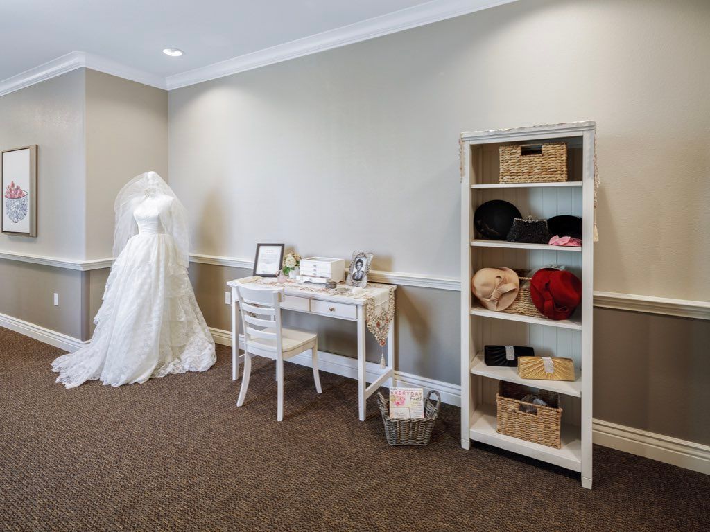 A room featuring a bridal gown on display, a vanity table with photo frames, and a shelving unit with neatly arranged baskets.