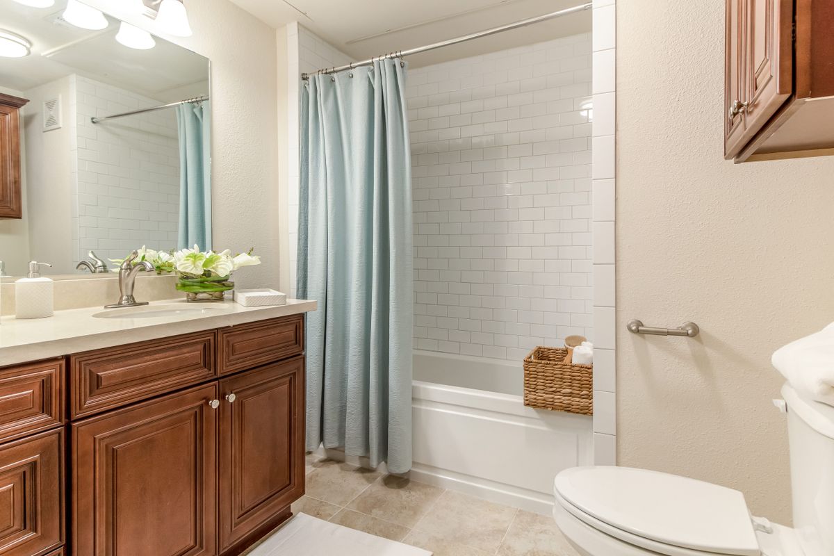 A clean and neat bathroom featuring a wooden cabinet, blue shower curtain, and a decorative basket on the tub.