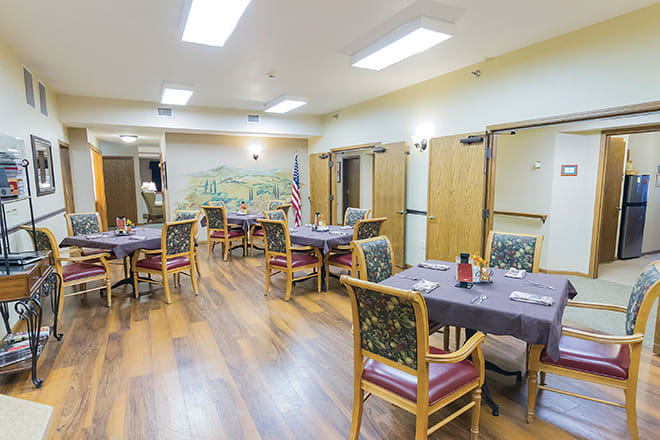 An indoor dining area with multiple tables and chairs arranged neatly on a wood floor.