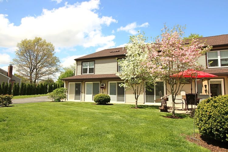A spacious two-story house with a lush green lawn and blossoming trees under a partly cloudy sky.