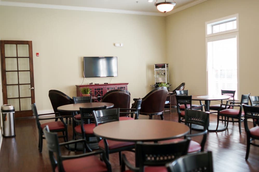 A lounge area with several round tables and chairs, featuring a wall-mounted television.