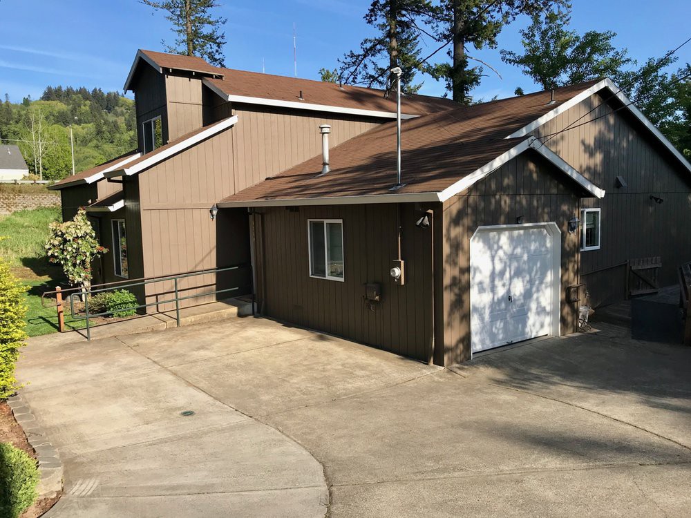 A two-story house with a driveway and garage, surrounded by trees under a clear blue sky.