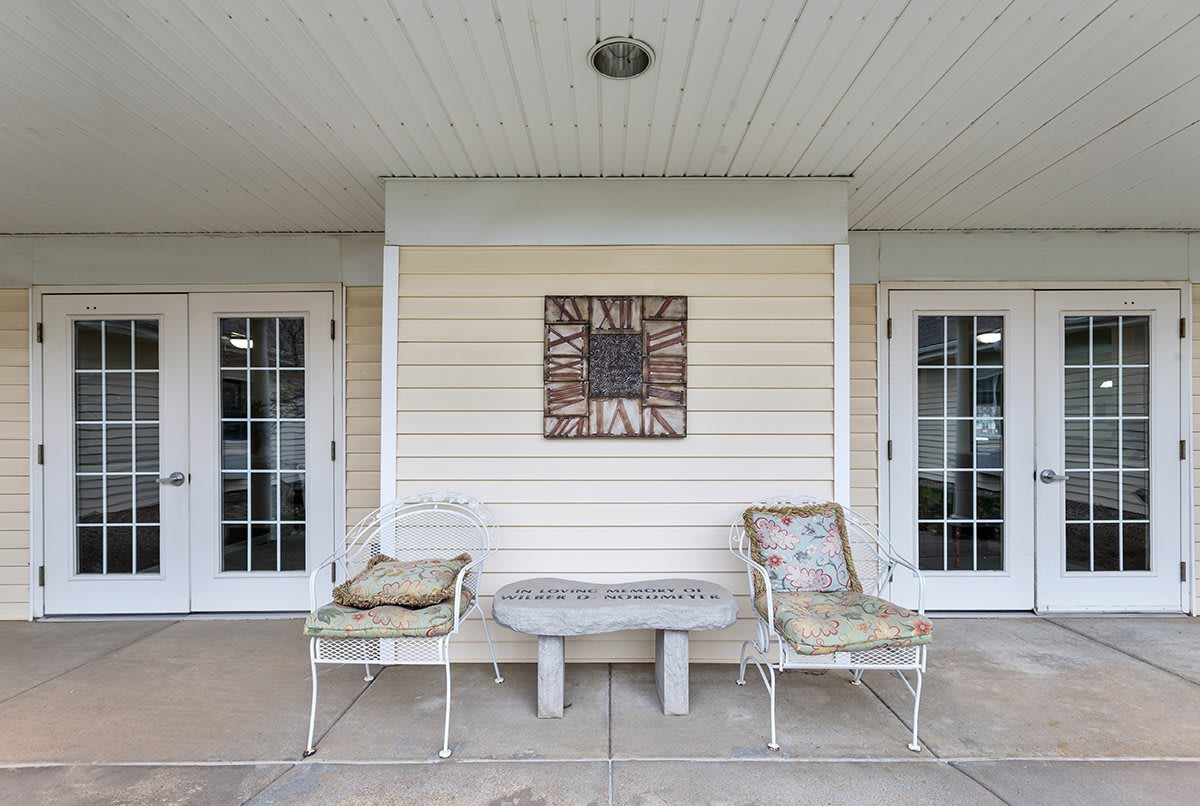 A cozy patio setup with two chairs, a small table, and decorative wall art between double doors.