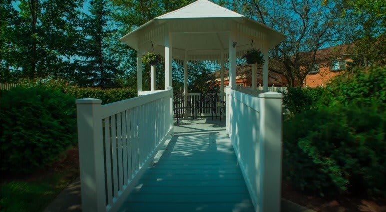 A scenic view of a white gazebo with a wooden walkway surrounded by greenery.