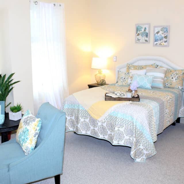 A cozy and well-decorated bedroom with a neatly made bed, bedside lamp, and comfortable seating area.