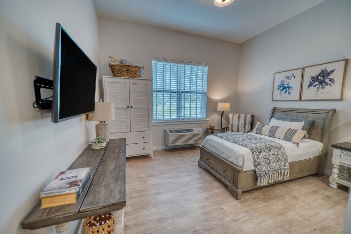 A cozy and well-decorated bedroom featuring a comfortable bed, a large television, a dresser, and bedside lamps.