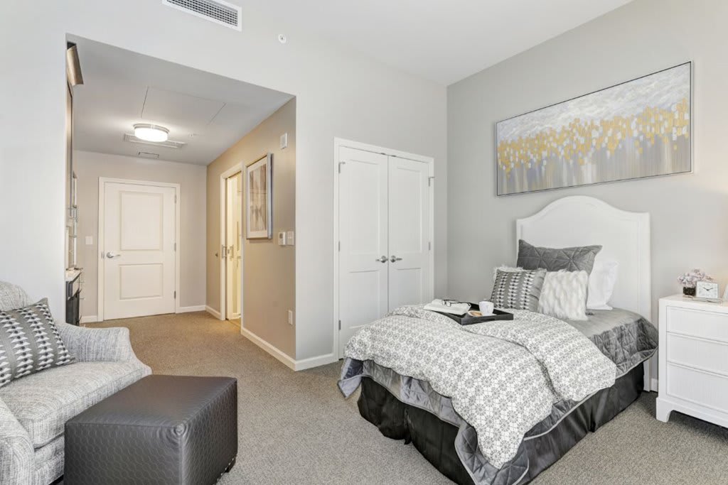 A modern and cozy bedroom featuring a neatly made bed with gray and white bedding, accented by a wall painting and soft lighting.