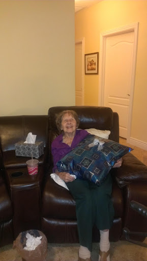 An elderly woman happily sitting on a couch with decorative pillows.