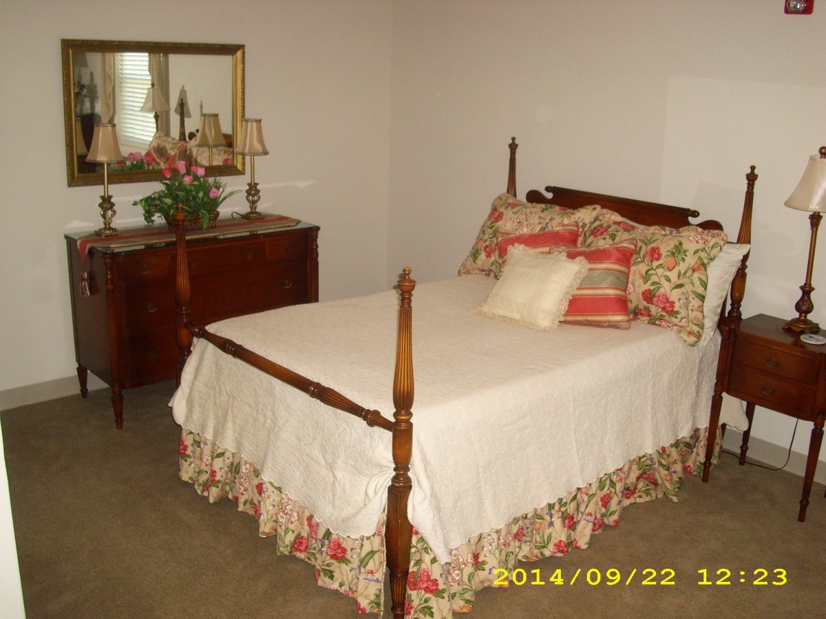 A cozy bedroom with a wooden bed and dresser, featuring floral bedding and decorative cushions.
