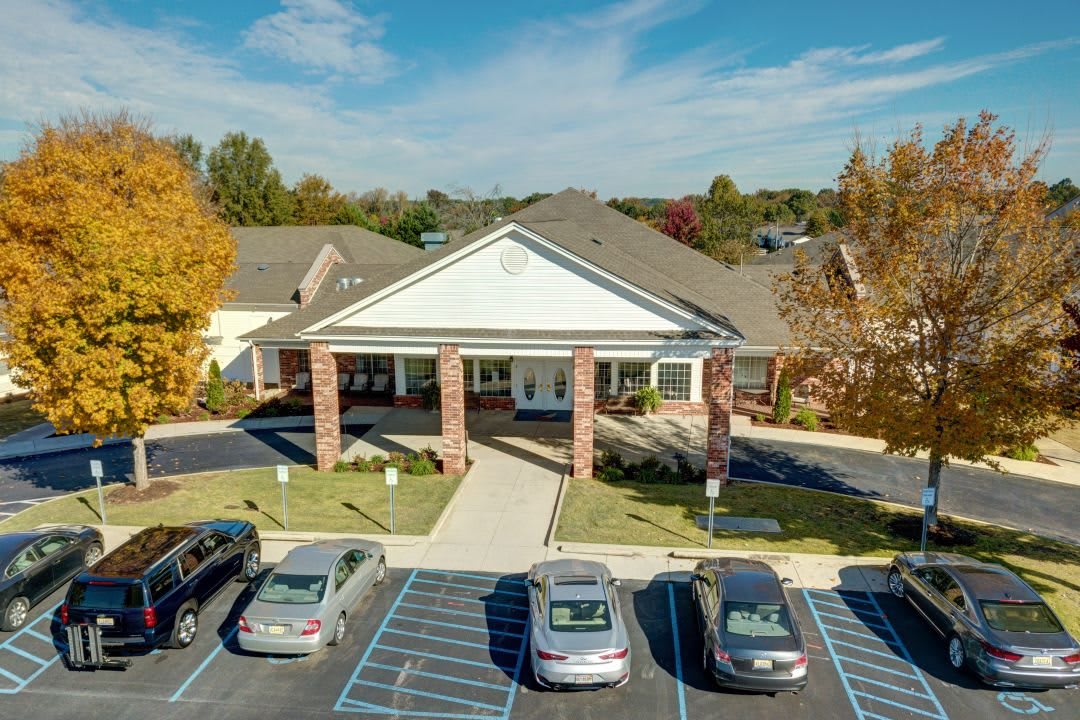 Aerial view of a building with a parking lot in front, surrounded by autumn trees.