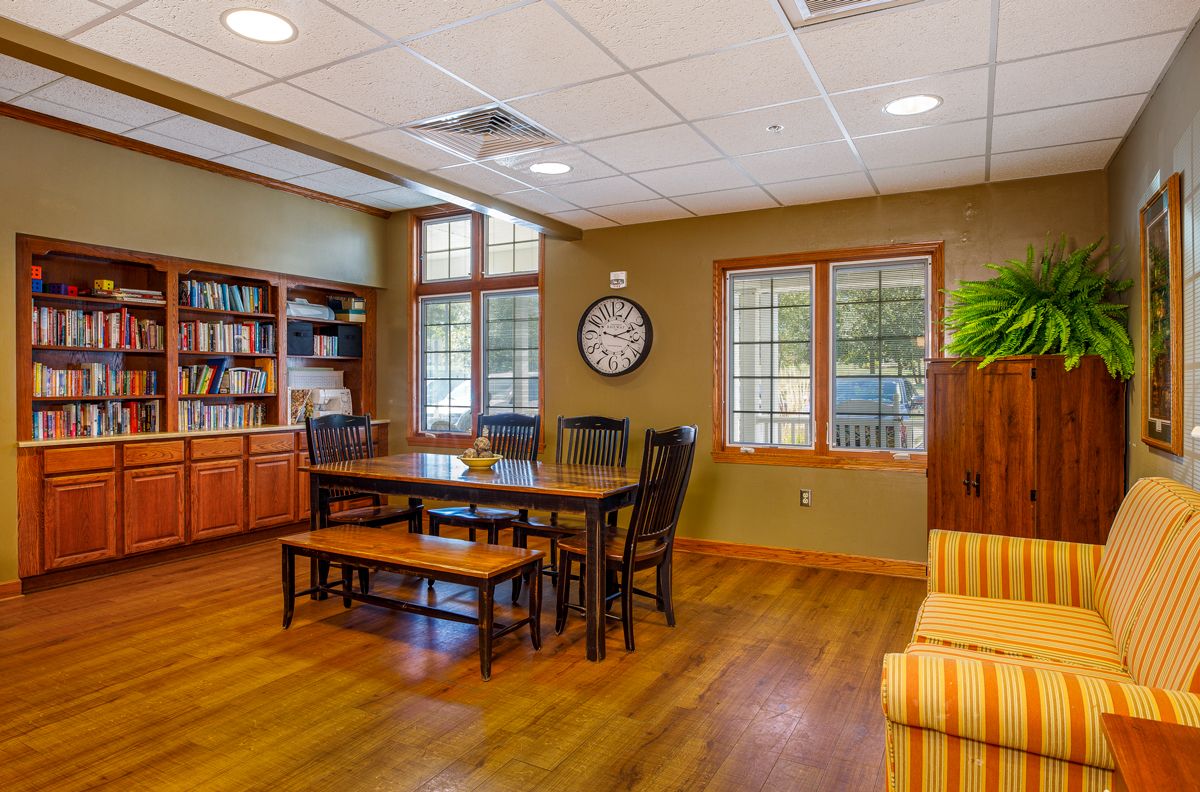 A cozy office interior with a wooden table, chairs, and a bookshelf.