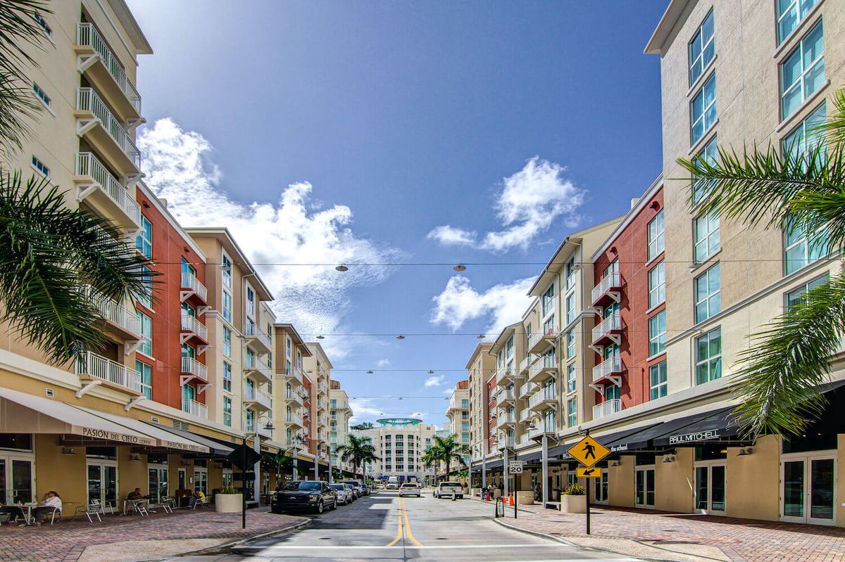 A vibrant city street lined with modern buildings and palm trees under a clear blue sky.