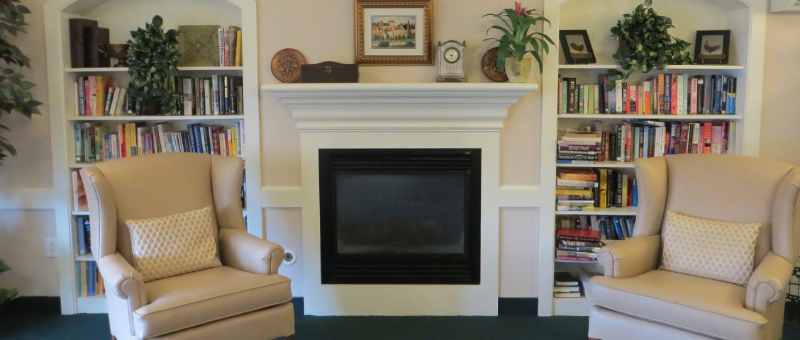 A cozy living room featuring a stylish fireplace with a decorated mantel, adjacent to a bookshelf and comfortable chair.