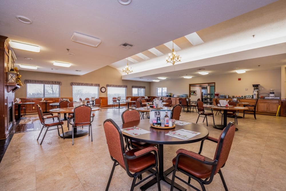 A spacious dining area with neatly arranged tables and chairs, featuring large windows and overhead lighting.