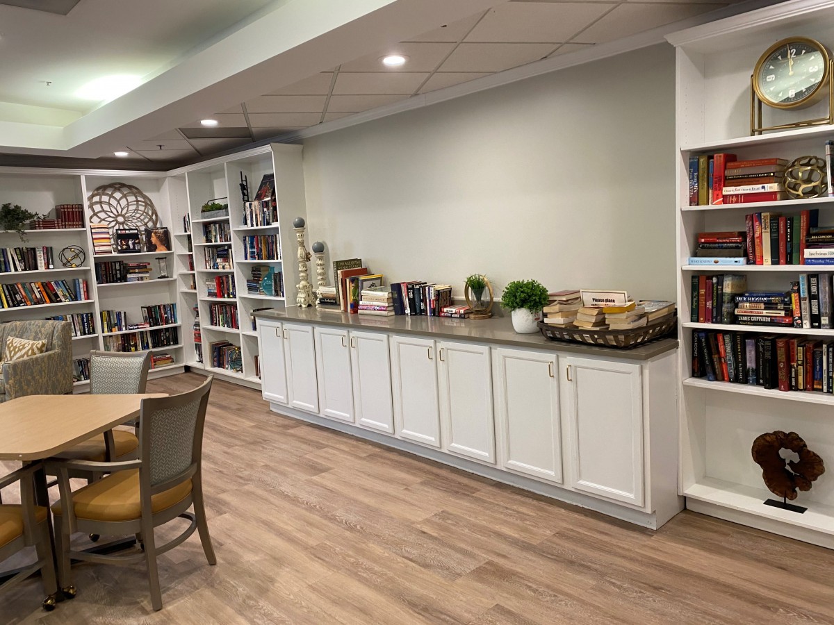 A cozy library with bookshelves and a reading area, featuring a long cabinet and wooden flooring.