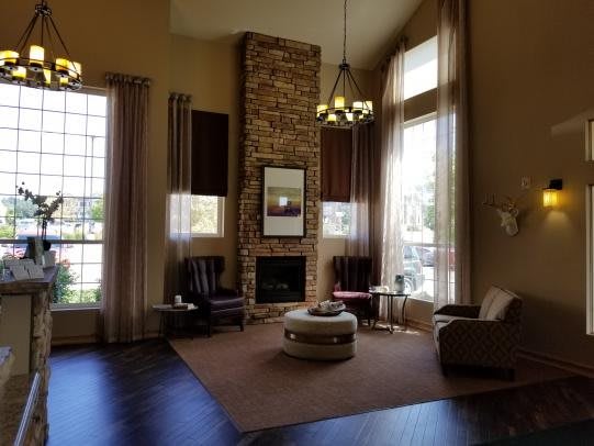 A spacious living room featuring a stone fireplace, large windows with curtains, and a cozy seating area with armchairs and a coffee table.