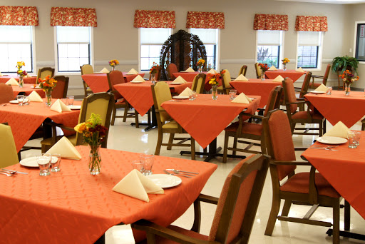 A well-decorated dining room with orange tablecloths and floral centerpieces, ready for guests.