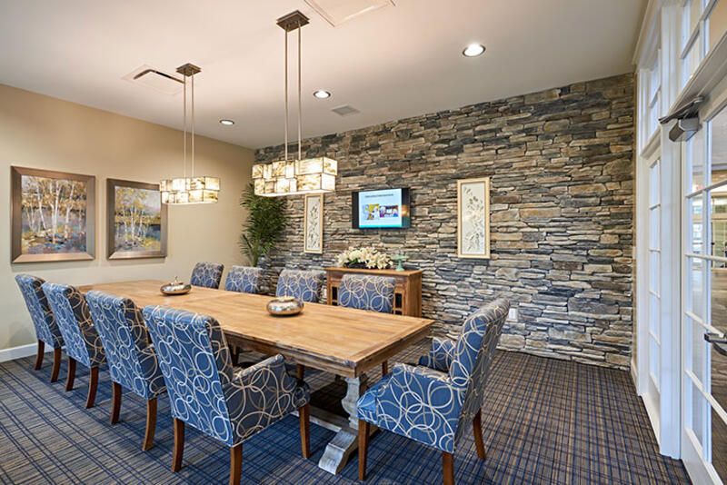 A modern dining or conference room featuring a stone accent wall, a large wooden table surrounded by upholstered chairs, and elegant lighting fixtures.