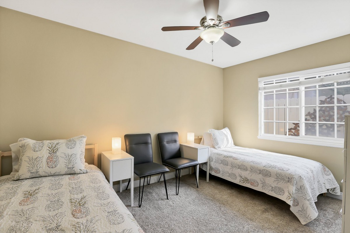 A cozy bedroom with two twin beds, bedside tables with lamps, and a ceiling fan.