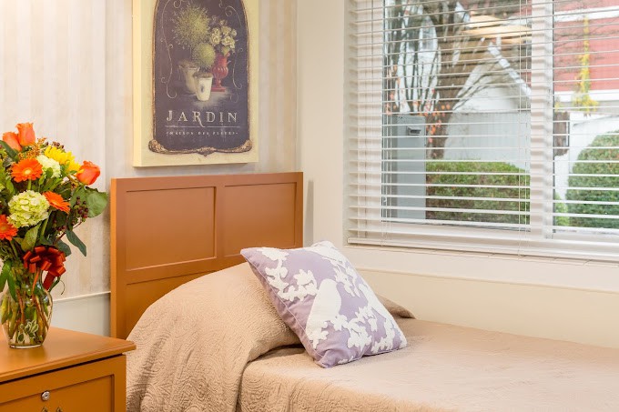 A cozy single bedroom with a pillow on the bed, a poster on the wall, and a window allowing daylight in.