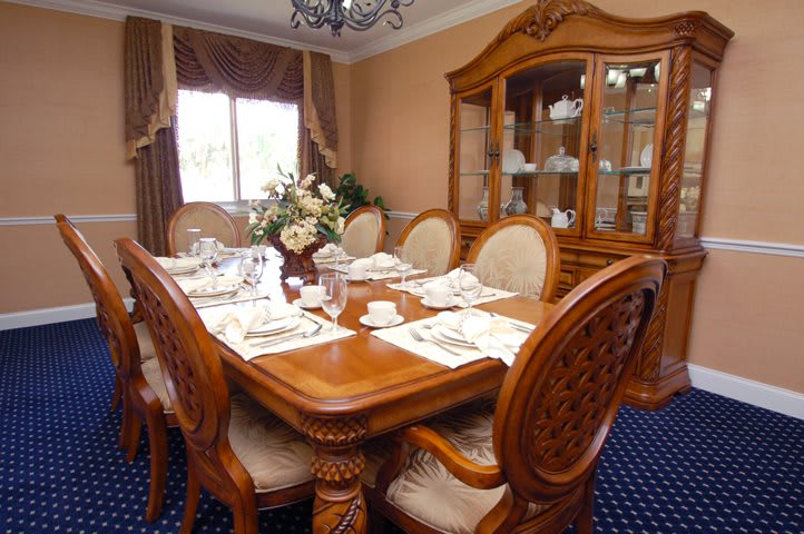 A traditional dining room with a wooden table and chairs, elegantly set for a meal, featuring a china cabinet and decorative curtains.