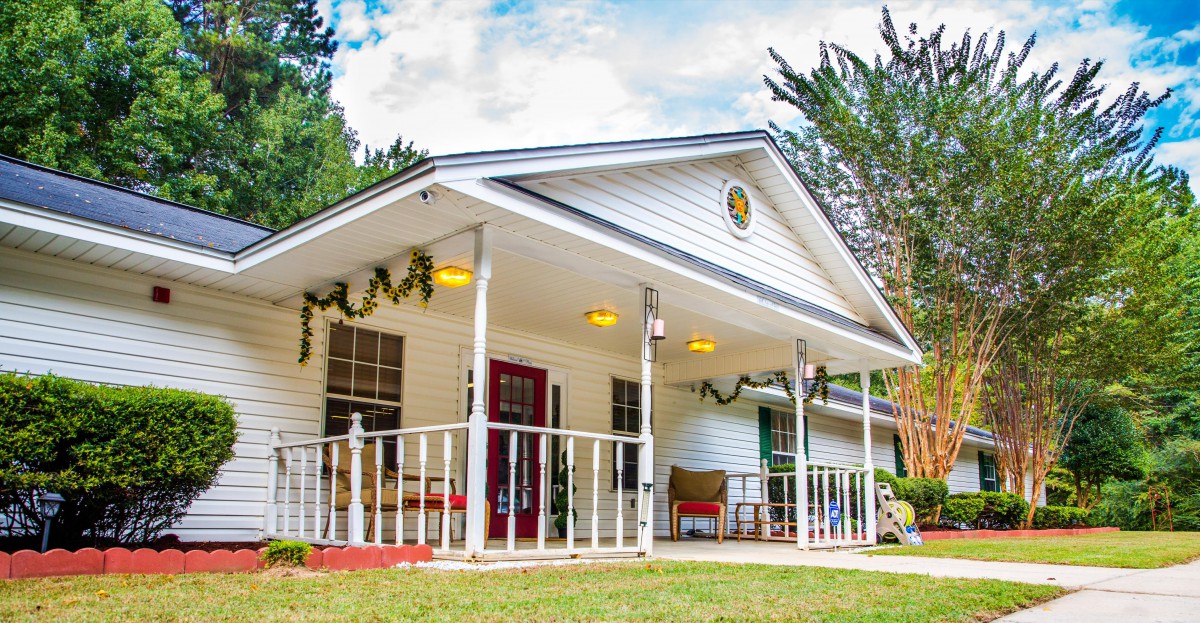 A charming white cottage with a welcoming porch surrounded by lush greenery.
