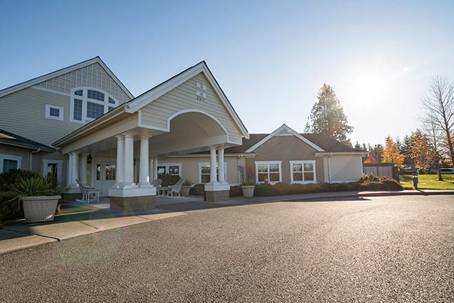 A large, modern residential building with a covered entrance and a spacious driveway under clear skies.