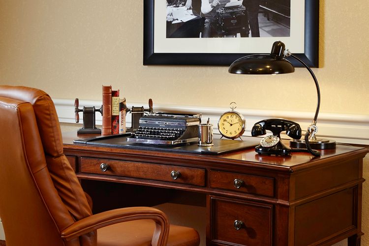 A vintage office setup featuring a wooden desk with a typewriter, classic telephone, and an old-fashioned clock.