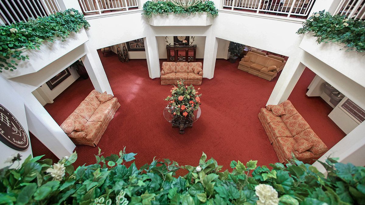 A spacious lobby with red carpeting, decorated with sofas, plants, and a central floral arrangement.